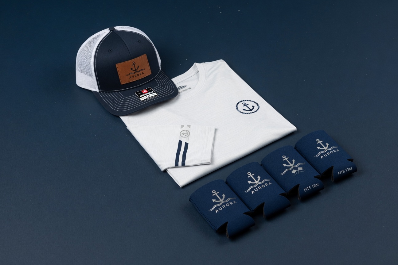 Example Crew Essentials bundle: trucker hat with patch, long sleeve tee, and custom koozies isolated on #F5F1E7 cream background